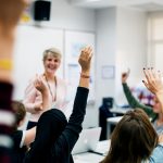 Students with their hands up responding to their teacher