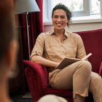 Overjoyed therapist making notes and looking at her female patient while laughing out loud